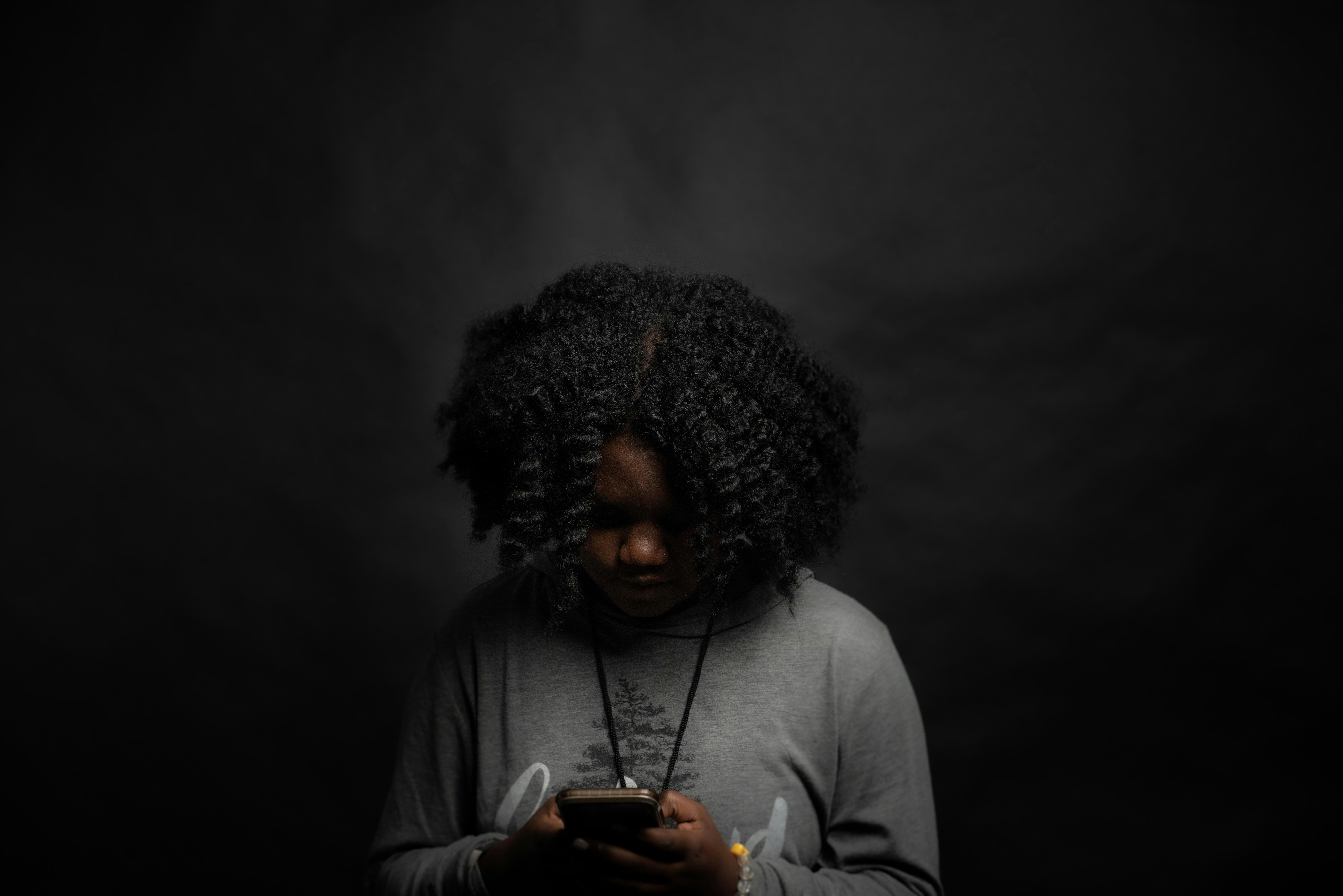 Woman looking down at her phone in a dark room, upset
